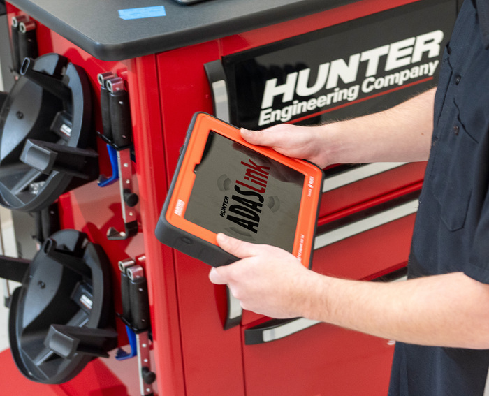 Technicien utilisant l’outil de diagnostic ADASLink dans un atelier automobile.