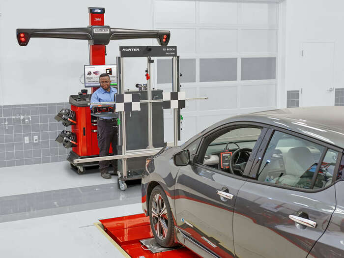 Technician operating Bosch DAS 3000 Static Calibration Fixture in front of vehicle at auto shop, showing ADAS setup process.