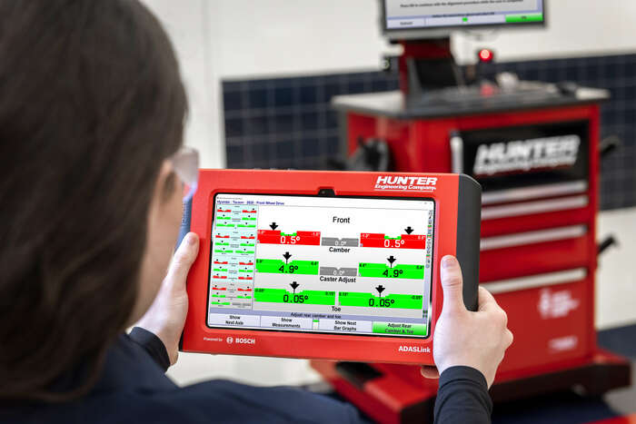 Technician using ADASLink screen mirroring feature to view camber and toe measurements from WinAlign console.